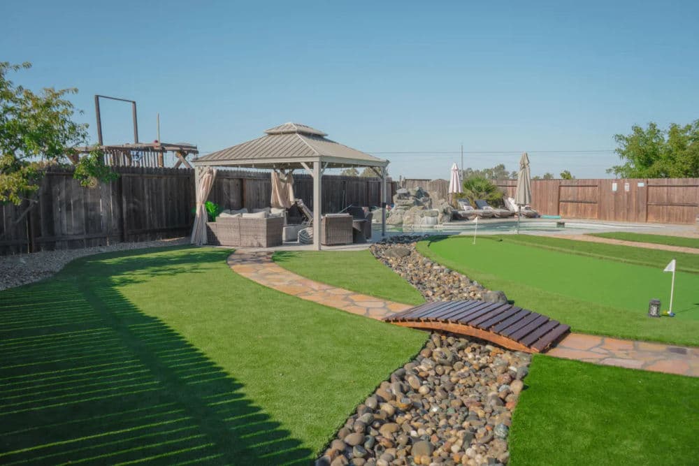 Lush backyard with gazebo, stone pathway, and putting green in sunny outdoor space.